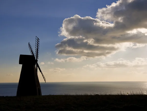 Silhueta de moinho de vento soprando nuvens escuras para revelar a explosão do sol — Fotografia de Stock