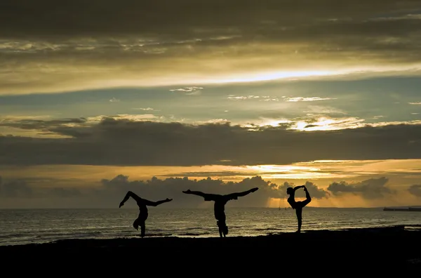 Silhouette of three young fit girls doing exercises on beach at — Stock Photo, Image