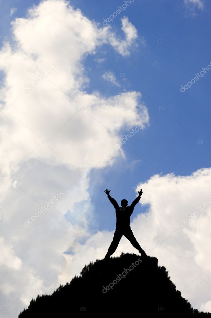 Silhouette of man on top of peak stretching arms towards sky in