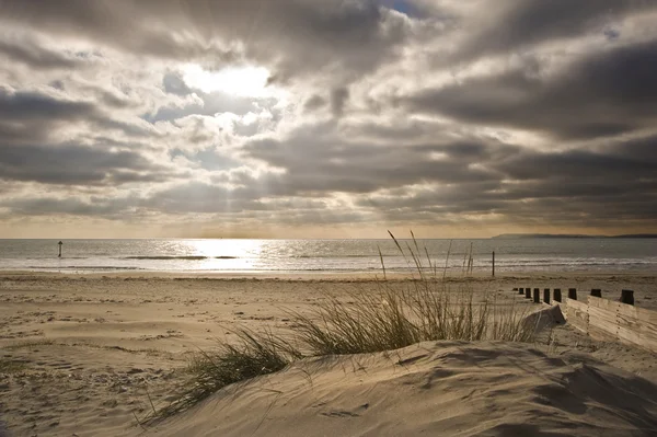 Приголомшливе надихаюче зображення заходу сонця з сяючими сонячними променями над трав'янистим піском — стокове фото