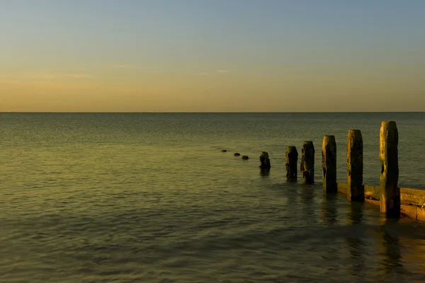 Peaceful sunrise over smooth sea with wooden groyne jetty — Stock Photo, Image