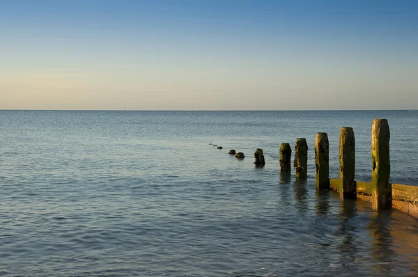 Peaceful sunrise over smooth sea with wooden groyne jetty — Stock Photo, Image