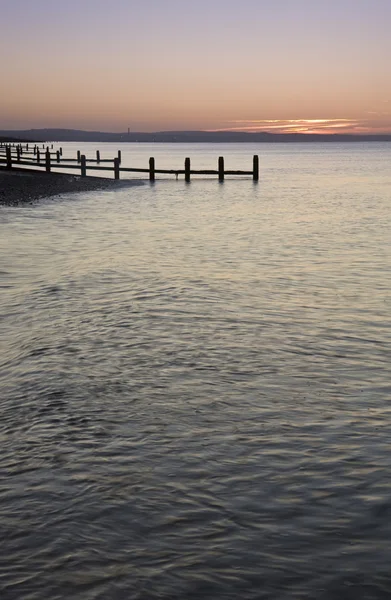 Vreedzame zonsopgang boven glad zee met houten krib steiger — Stockfoto