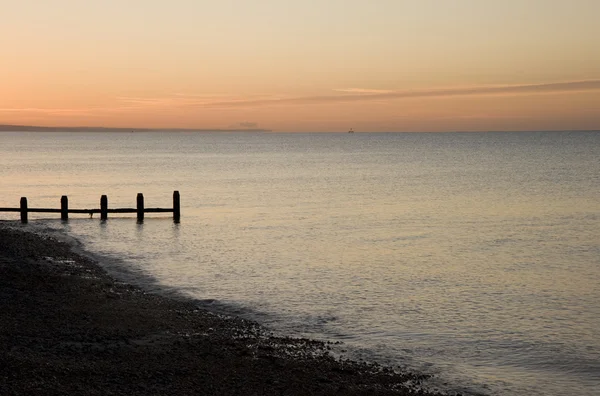 Nascer do sol pacífica sobre o mar liso com madeira groyne molhe — Fotografia de Stock