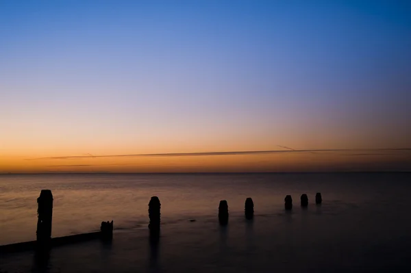Amanecer pacífico sobre mar liso con espigón de madera del groyne — Foto de Stock