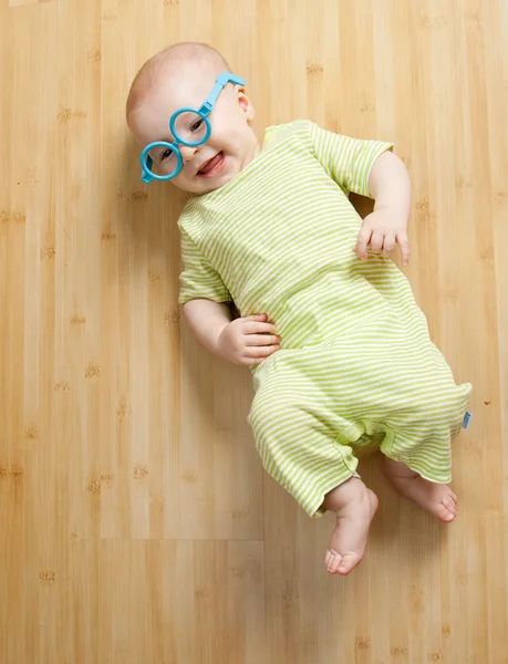Kleiner Junge in lustiger Spielzeugbrille liegt auf dem Boden — Stockfoto