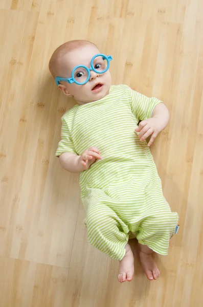 Kleiner Junge in lustiger Spielzeugbrille liegt auf dem Boden — Stockfoto