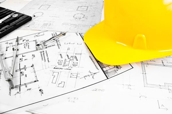 Angle shot de algunos planos de construcción y un casco amarillo — Foto de Stock