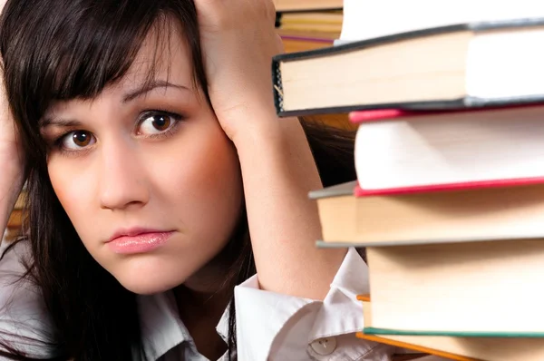 Jovem estudante menina segurando a cabeça atrás de um monte de livros — Fotografia de Stock