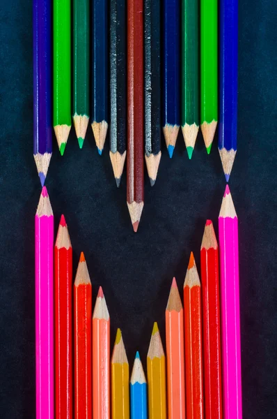 Bir kalp şeklinde koyu arka plan üzerinde renkli kalemler — Stok fotoğraf