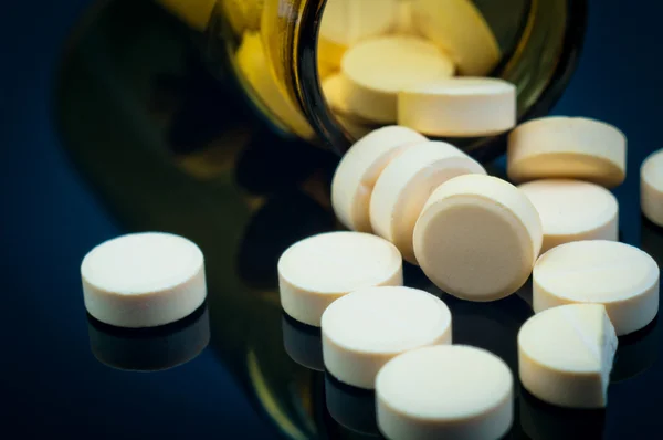 Pílulas médicas fora de sua garrafa em fundo preto — Fotografia de Stock