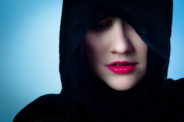 Dívka v černých kapucí proti modré pozadí — Stock fotografie