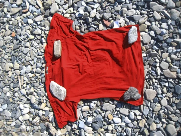 Красная футболка лежала на берегу под четырьмя камнями — стоковое фото