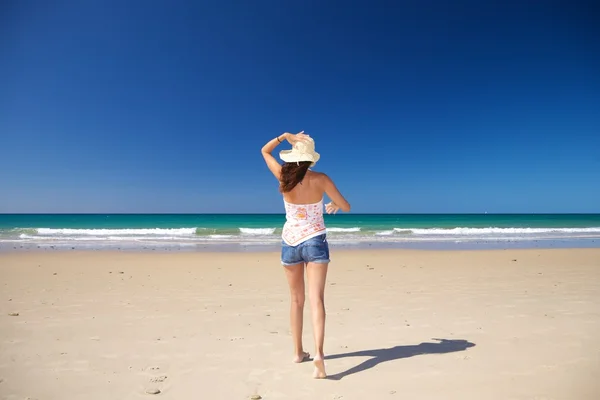 Walking holding on straw hat at beach — Stock Photo, Image