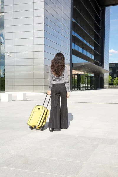 Kobieta z żółtym walizkę przed budynkiem firmy — Zdjęcie stockowe