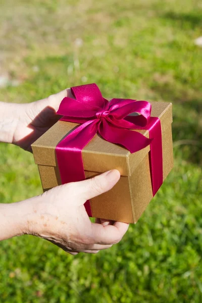 Granny hands with gift box on green background — Stock Photo, Image