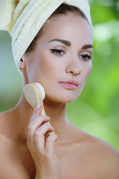 Jovem mulher bonita limpa o rosto com uma escova macia — Fotografia de Stock