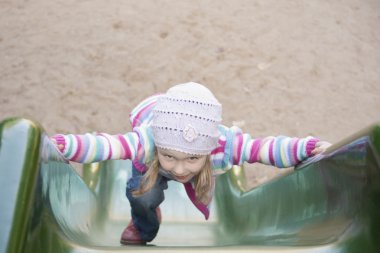 Happy girl climbing on children's slide clipart