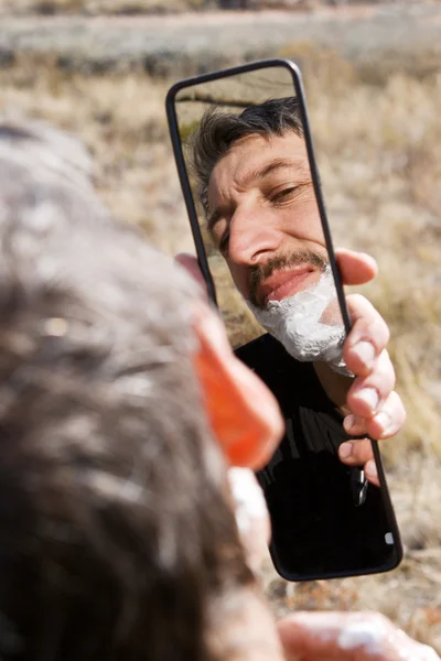 Чоловік голиться, дивлячись в автомобільне дзеркало — стокове фото