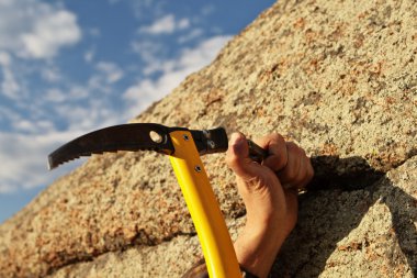 Hands rock-climber hammering in hook in rock clipart