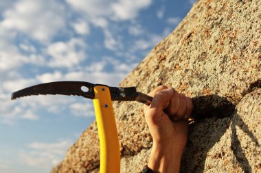 Hands rock-climber hammering in hook in rock clipart