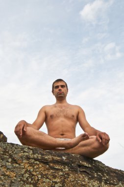 Good-looking young man doing yoga on stone