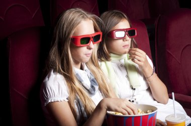 Two beautiful girls watching a movie at the cinema clipart