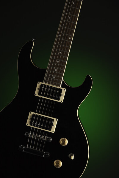 A black electric guitar isolated against a spotlight green background