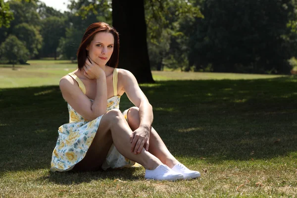 Mooie jonge vrouw zittend op het gras in park — Stockfoto