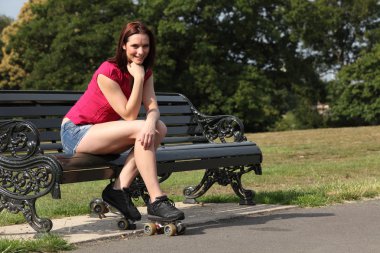 Cheerful skater girl sitting in sun on park bench clipart