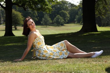 Happy young woman tanning in park summer sunshine clipart