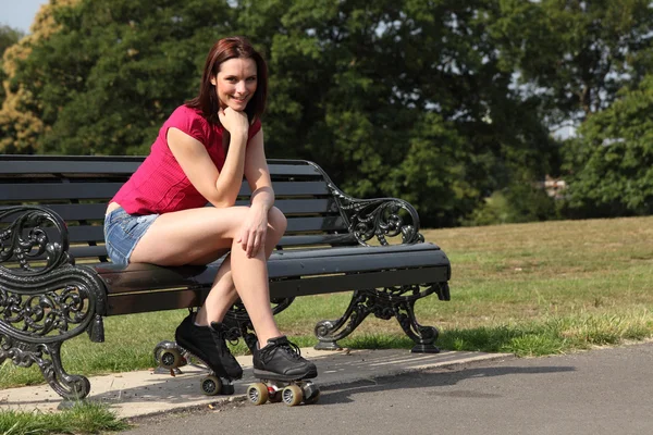 Весела дівчина ковзаняра сидить на сонці на лавці парку — стокове фото