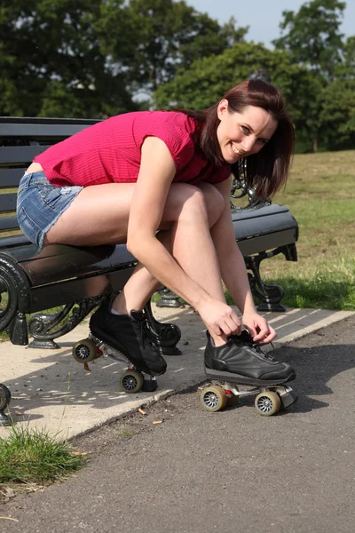 Beautiful girl ties roller skates on park bench — Stock Photo, Image