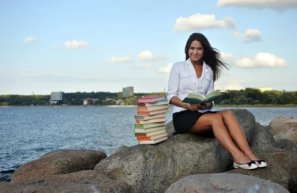 Κορίτσι με βιβλία κάθεται σε έναν βράχο δίπλα στη θάλασσα — Φωτογραφία Αρχείου