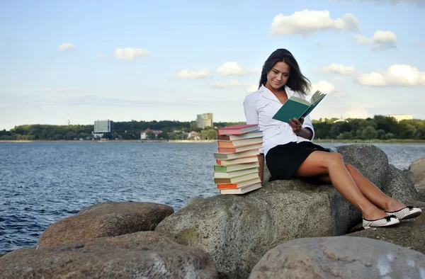 Ragazza con libri seduta su una roccia in riva al mare — Foto Stock