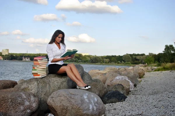 Девушка с книгами, сидящая на скале у моря — стоковое фото