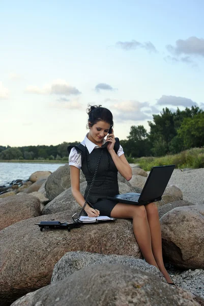 Oficina junto al mar: la chica en las rocas con un ordenador portátil y un teléfono de escritorio —  Fotos de Stock