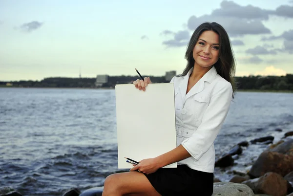 A szép lány a gazdaság üres papír fehér kabátot. tenger a háttérben — Stock Fotó