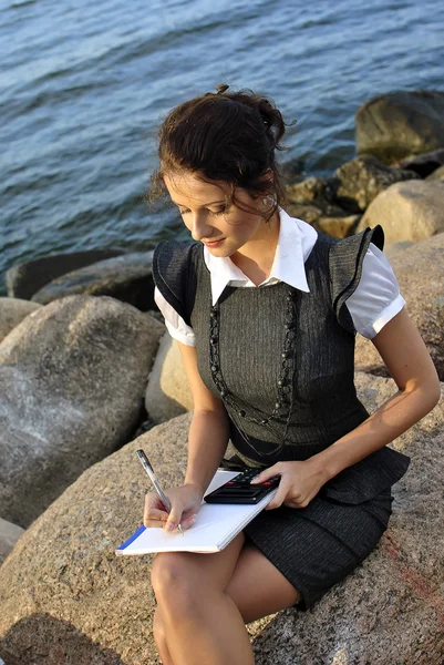 Όμορφο κορίτσι με ένα σημειωματάριο και μια αριθμομηχανή που κάθονται πάνω στα βράχια — Φωτογραφία Αρχείου