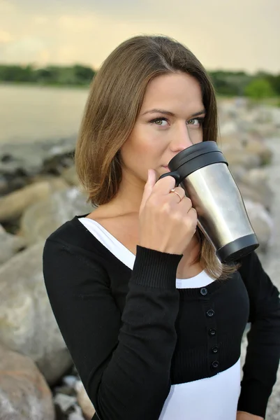 Beautiful girl standing on the beach with a mug of coffee — Stock Photo, Image