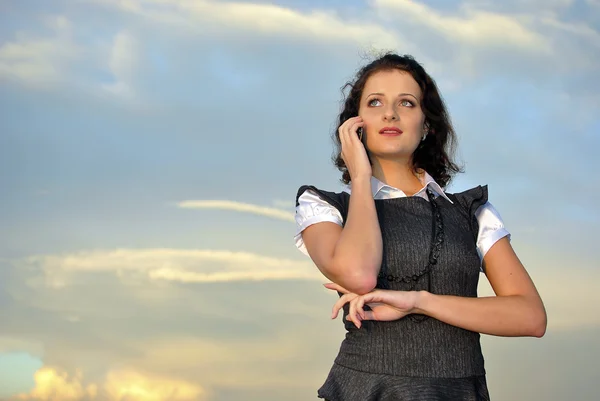 Vacker flicka med en mobiltelefon. Sky på bakgrund — Stockfoto
