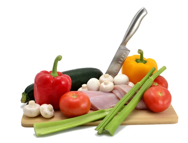 Pollo, cuchillo y verduras en una tabla de cortar, aislados en blanco — Foto de Stock