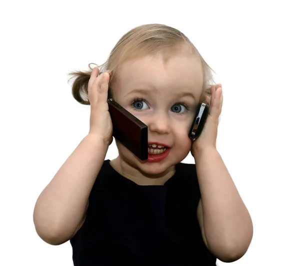 Забавная маленькая девочка разговаривает по двум телефонам, изолированная на белом — стоковое фото