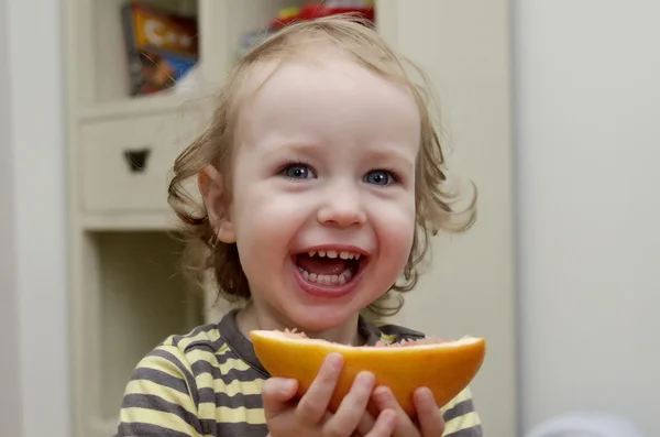 Little girl laughing and eating grapefruit — Stock Photo, Image