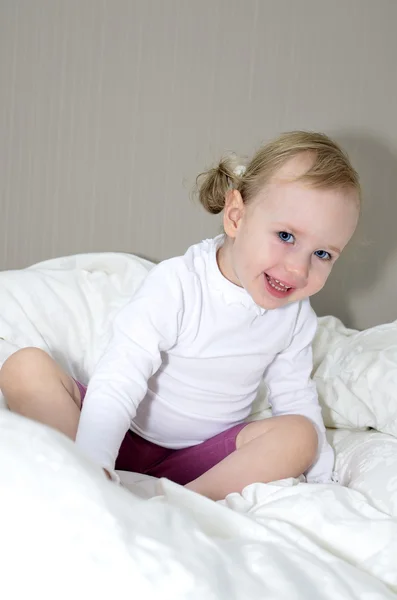 Menina sentada em uma cama e sorrindo — Fotografia de Stock