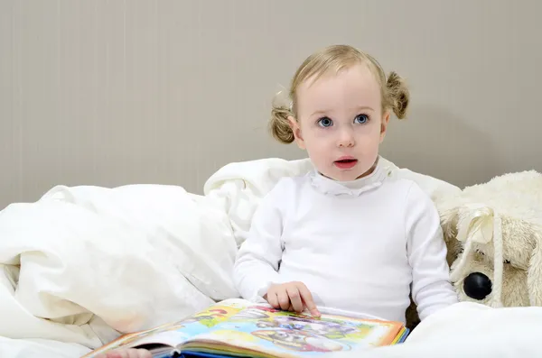 Meisje, zittend op het bed en lezen van een boek — Stockfoto