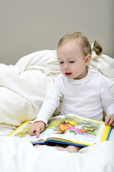 Menina sentada na cama e lendo um livro — Fotografia de Stock