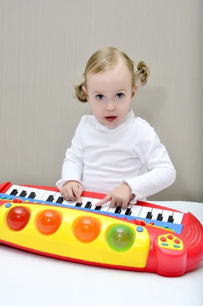 Menina sentada na cama e brinca com um teclado infantil — Fotografia de Stock