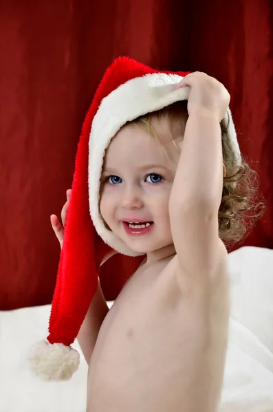 Dziewczynka w Boże Narodzenie czerwony kapelusz siedzi na łóżku — Zdjęcie stockowe
