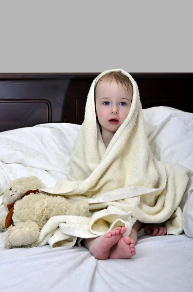 Klein meisje in een handdoek na een douche rusten op een bed — Stockfoto